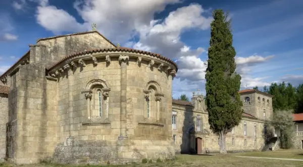 Antigua iglesia románica en Ferreira de Pantón, Lugo. Fachada de piedra con arcos y un ciprés alto.