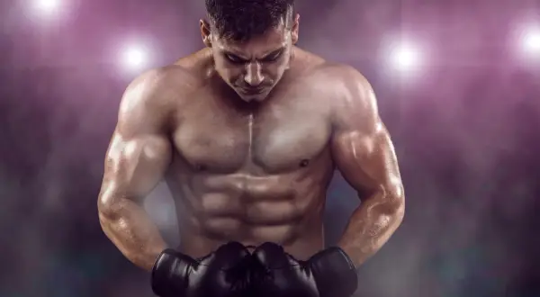 A muscular boxer with a defined boxer physique, wearing black gloves, looks down intensely under stadium lights.
