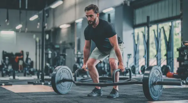 Un homme concentré effectue un dead lift avec une barre hexagonale dans une salle de sport.