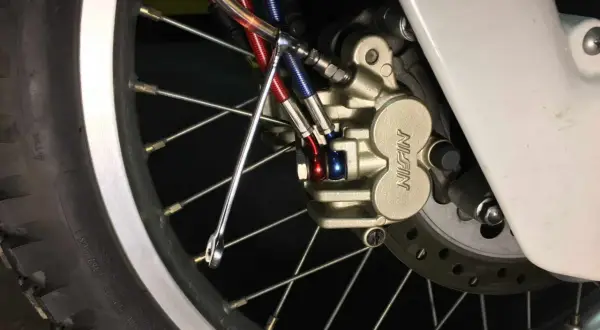 Zbliżenie na zacisk hamulcowy motocykla z przewodami hamulcowymi i kluczem.