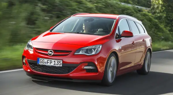 Czerwona Astra J 1.7 CDTI w wersji kombi pędzi po krętej drodze wśród zieleni.
