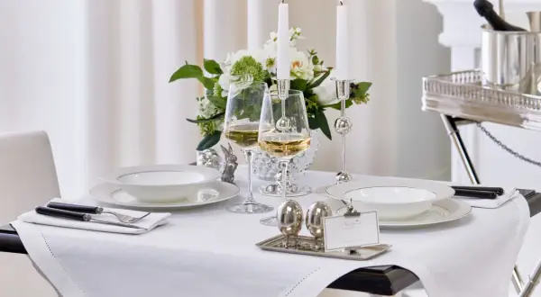 Vacker dukning med vita tallrikar, vinglas och ljus. Frågan "hur stor duk ska man ha" besvaras här med en duk som täcker bordet elegant.