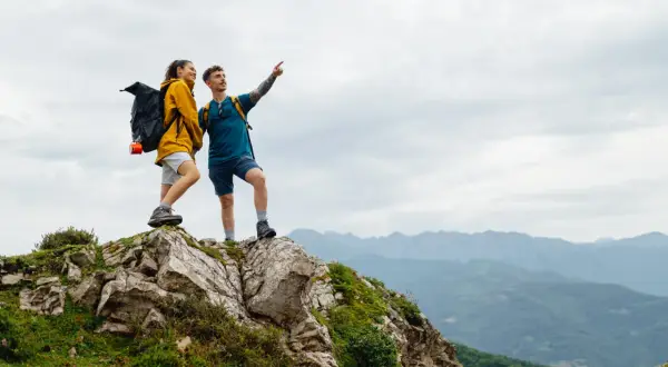 Zwei Wanderer auf einem Felsvorsprung genießen die Aussicht während ihrer Alpen Tour.