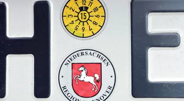 Fragment niemieckich tablic rejestracyjnych z literami H i E, naklejkami z regionu Hanower i datą przeglądu.