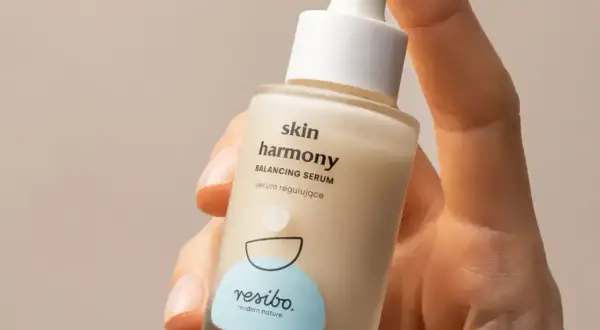 Dłoń trzyma buteleczkę serum Resibo Skin Harmony. Składnik alantoina wspiera regenerację skóry.
