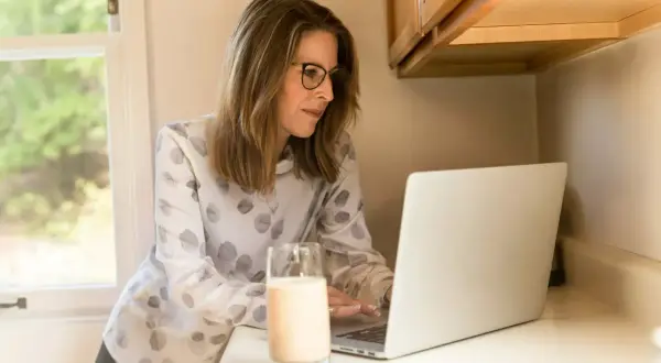 Frau mit Brille am Laptop, studieren mit 40 berufschancen. Ein Glas Milch steht daneben.