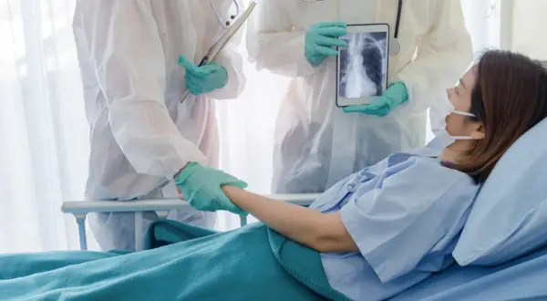 Lekarze w kombinezonach ochronnych wspierają pacjentkę w szpitalu, pokazując jej zdjęcie płuc na tablecie. Nadzieja na powrót do zdrowia dzięki leczeniu, być może z użyciem remdesivir.
