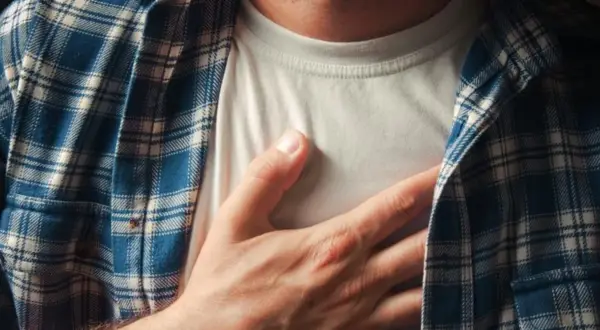 Dłoń na piersi, odczuwając niepokojący ucisk w klatce piersiowej. Mężczyzna w koszuli w kratę.