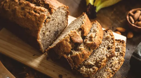 Saftiges Bananenbrot, perfekt für ein Bananenbrot Rezept ohne Zucker. Daneben liegen Mandeln und reife Bananen.