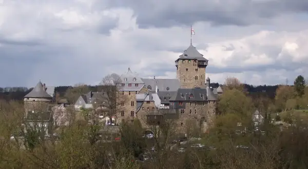 Das Schloss Burg an der Wupper, eine imposante Burganlage mit Bergfried und vielen Gebäuden, thront über Bäumen.