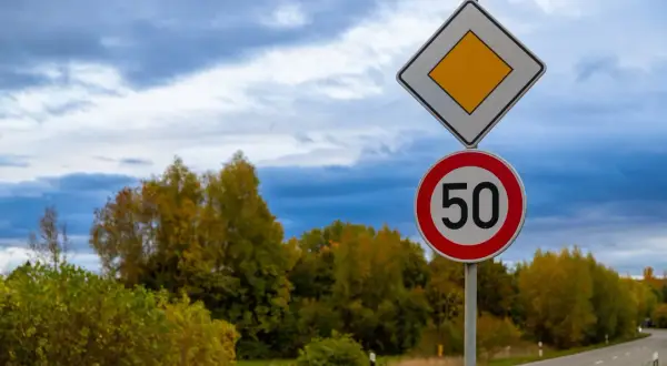 Panneau de priorité à droite et limite de vitesse à 50 km/h sur une route bordée d'arbres aux couleurs d'automne.