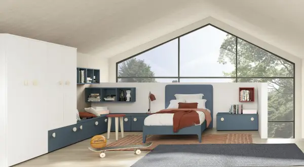 Un accogliente **letto sotto la finestra** in una stanza moderna con armadio bianco, librerie blu e dettagli sportivi come pallone e skateboard.