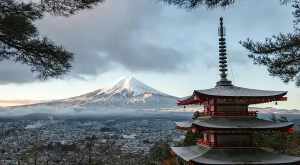 Japanische Regenzeit: Ein schneebedeckter Fuji-san erhebt sich über einer Stadt, daneben eine rote Pagode.