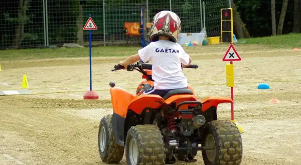 Dziecko w kasku na quadzie uczy się zasad ruchu drogowego na torze. To jego pierwsza karta motorowerowa.