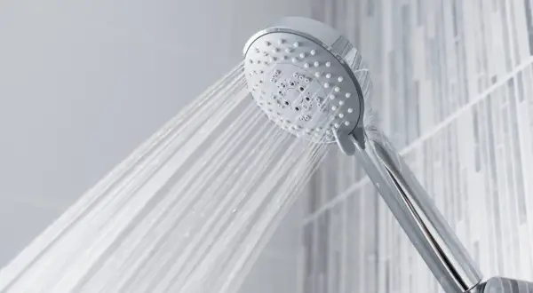 A chrome shower head sprays water, questioning if shower heads are universal.