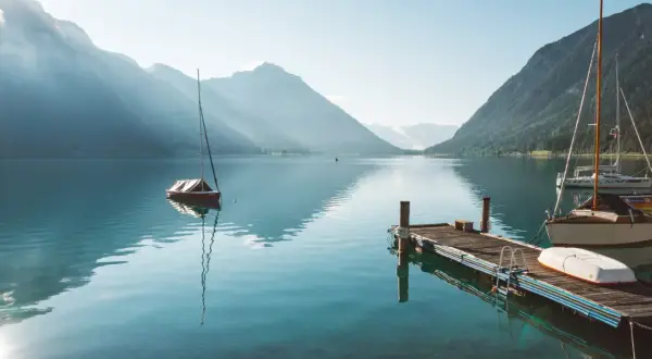 Segelboote am Achensee, ein wahrer Geheimtipp. Berge spiegeln sich im klaren Wasser, ein Steg lädt zum Verweilen ein.