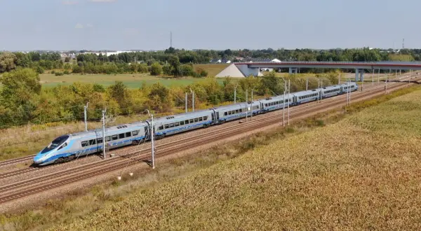 Nowoczesny pociąg Pendolino pędzi po magistrali kolejowej, mijając pola kukurydzy i zielone drzewa.