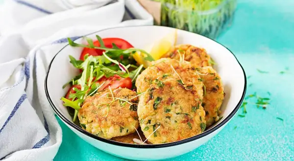 Croquetas de atún doradas y crujientes, servidas con una ensalada fresca de rúcula y tomate, y un toque de limón.