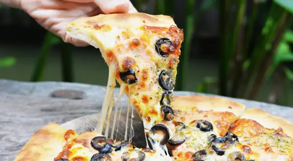 Ciągnący się ser z kawałka pizzy capriciosa z oliwkami, podnoszony ręką.