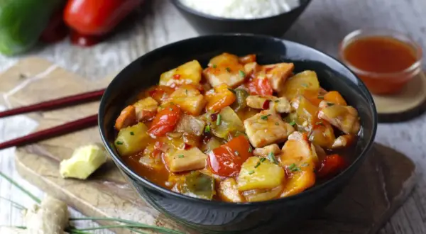 Sabroso wok de cerdo con trozos de piña, pimientos rojos y verdes, servido en un cuenco negro.