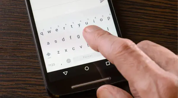 Dłoń pisze na smartfonie, klawiatura pokazuje brak polskich znaków w sms.