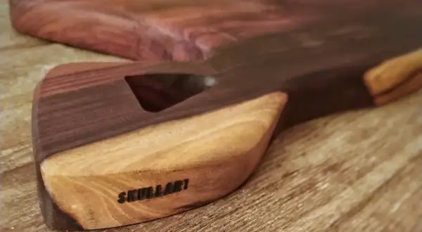 Tabla de cortar artesanal con veta de madera africana, marcada con "SKULLART".