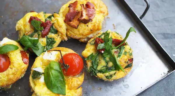 Matiga muffins med ägg, spenat, tomat och bacon på en plåt. Perfekt för en mättande frukost eller brunch.