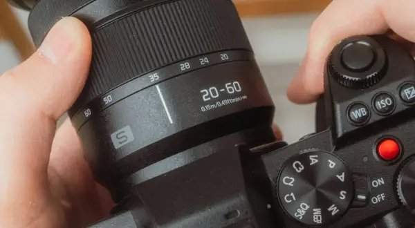 Dłonie trzymają aparat, obracając pierścień z oznaczeniami 20-60 mm. To właśnie zoom, czyli możliwość zmiany ogniskowej obiektywu.