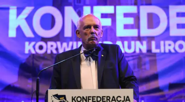 Mężczyzna w garniturze i muszce przemawia na tle napisu "KONFEDERACJA".
