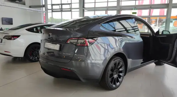Szary Tesla Model Y z otwartymi drzwiami, obok biały Model 3. Wymiary tego SUV-a są idealne do miasta i na dalsze trasy.