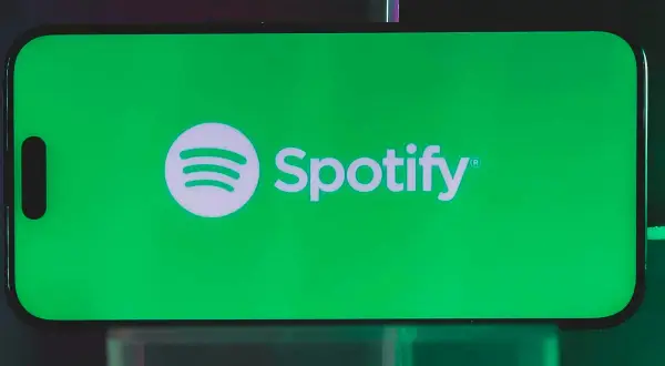 A smartphone displays the Spotify logo on a vibrant green screen, hinting at a free distributor for Spotify.