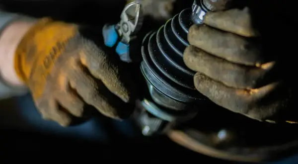 Mechanik w rękawicach naprawia przegub w samochodzie, używając szczypiec.