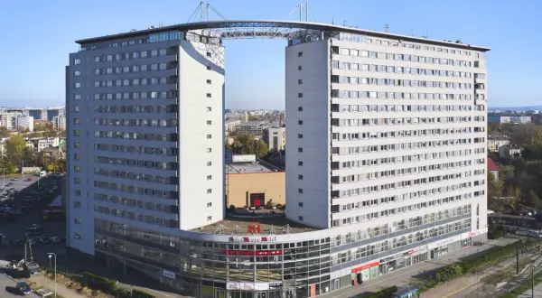 Dom wschodzącego słońca, nowoczesny budynek z charakterystycznym mostem łączącym dwie wieże, z widokiem na miasto.