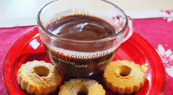 Bicchiere di cioccolata calda con acqua senza fecola, accompagnata da biscotti su un piatto rosso.