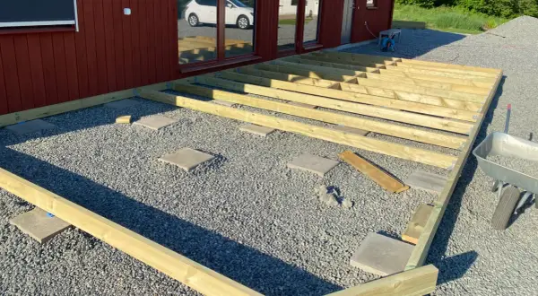 Bygga altan på plattor. Träkonstruktion för altan monteras på grusunderlag med stenplattor som stöd.