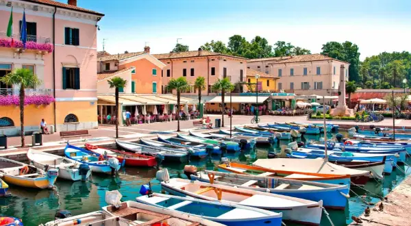 Barche ormeggiate nel **bardolino hafen**, con edifici colorati e palme sullo sfondo.