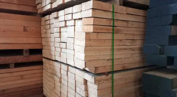 Piles of light-colored lumber, possibly madera ayous, are stacked high. A stack of dark wood is visible on the right.