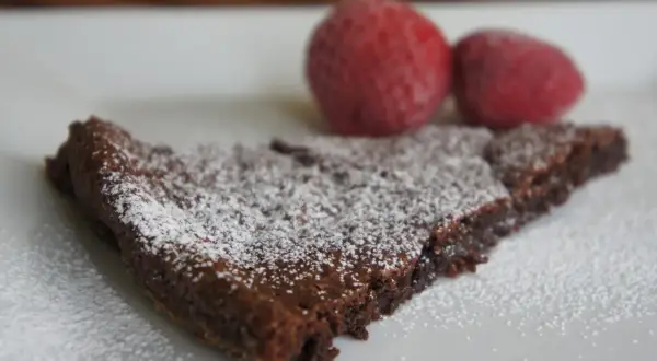 En bit kladdkaka, pudrad med florsocker, med två jordgubbar i bakgrunden. Perfekt för dig som älskar kladdkakecookies utan choklad.
