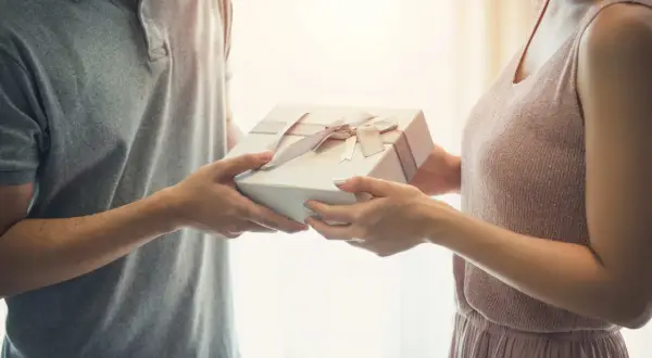 Mężczyzna wręcza kobiecie prezent z okazji 25 rocznicy ślubu. Delikatne wstążki zdobią pudełko.