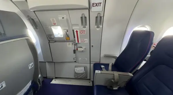Wnętrze samolotu Wizzair. Widok na rząd siedzeń i drzwi wyjściowe. Numeracja miejsc w samolocie Wizzair jest widoczna na siedzeniach.