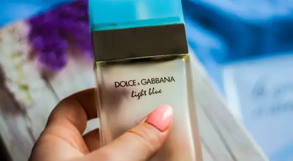 Dłoń z różowym lakierem trzyma buteleczkę perfum Dolce & Gabbana Light Blue.