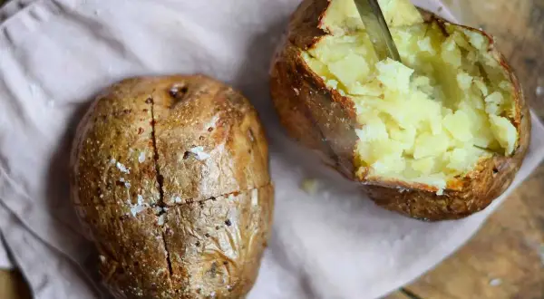 Perfekt bakad potatis i airfryer, en är uppskuren och visar det fluffiga inkråmet. Saltkorn glittrar på den gyllene ytan.