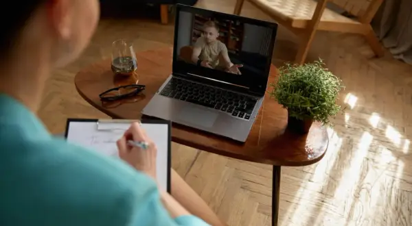 Kobieta prowadzi psychoterapię przez Skype, notując na bieżąco. Na ekranie laptopa widać mężczyznę w gabinecie.