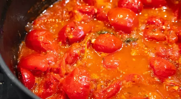 Frische, glänzende Tomaten köcheln in einer Pfanne zu einer aromatischen Tomatensauce.