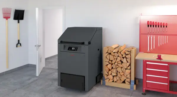 Holzstapel neben einem modernen Heizkessel, der bald dem Festbrennstoffkessel Verbot zum Opfer fallen könnte. Werkzeuge hängen an der Wand.