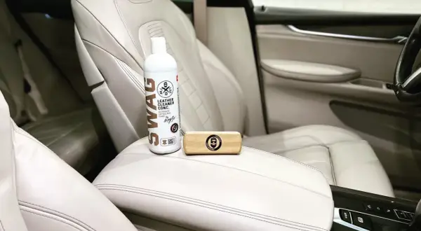 Zestaw do pielęgnacji jasnej skóry w samochodzie: butelka preparatu SWAG Leather Cleaner i drewniana szczotka. Idealne, by natłuścić skórę w samochodzie.