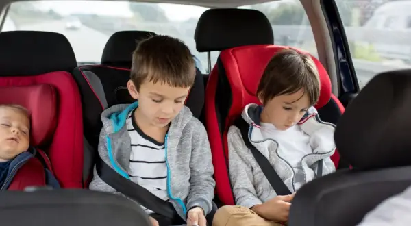 Im Auto mit 3 Kindern: Ein Baby schläft, die älteren Brüder sind mit ihren Handys beschäftigt.