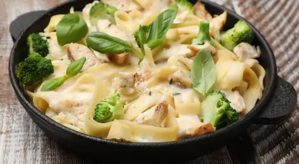 Pyszna potrawka z kurczaka z makaronem tagliatelle, brokułami i kremowym sosem, udekorowana świeżą bazylią.