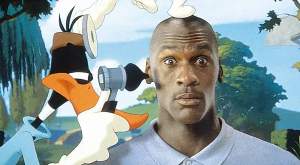 Michael Jordan z zaskoczoną miną, gdy Kaczor Daffy próbuje mu coś włożyć do ucha. Zabawna scena z komedii dla dzieci.