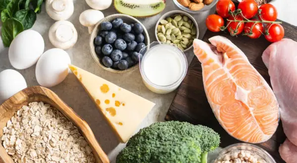 Vielfältige Lebensmittel für Muskelaufbau: Lachs, Hähnchen, Eier, Haferflocken, Beeren, Nüsse, Brokkoli, Käse und mehr.